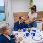 Operatrice domiciliare sorride e assiste una coppia di anziani in terrazza