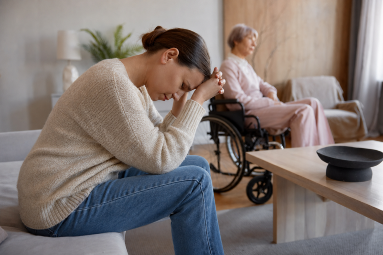 Caregiver affaticata accanto a una persona anziana in sedia a rotelle