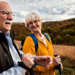 Coppia di anziani durante una passeggiata all’aperto tra colline e natura, in un momento di benessere e vitalità