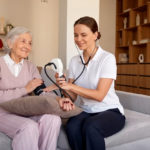 Infermiera a domicilio misura la pressione a un’anziana seduta sul divano durante un servizio di assistenza domiciliare.