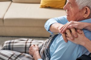 Caregiver appoggia le mani sulle spalle di un anziano seduto in casa durante un momento di supporto emotivo e assistenza domiciliare.